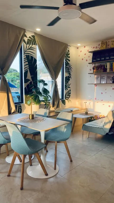 A window table with pale aqua chairs beside a hand-painted palm-leaf mural