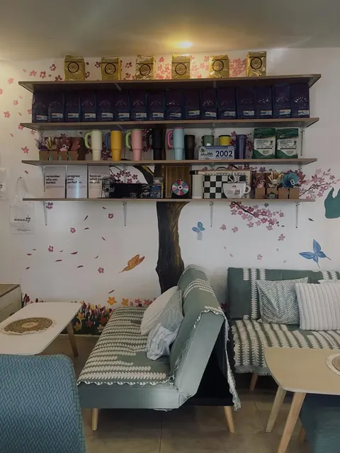 Sofas under a painted cherry blossom tree, with shelves of coffee bags, tumblers and gifts