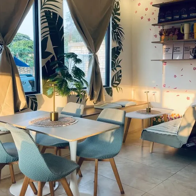 A window table with pale aqua chairs beside a hand-painted palm-leaf mural